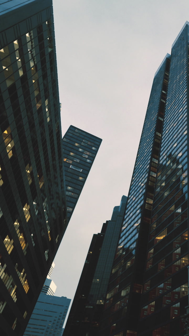 Tall buildings stretch upwards reflecting light against a soft dusk sky