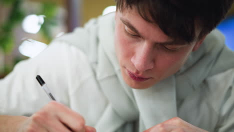 young boy wearing white polo leaning over sketchbook with intense focus on pencil strokes capturing moment of creative concentration under soft indoor light while observing every line quietly