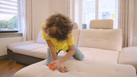 Blond-Boy-With-Curly-Hair-Kneeling-On-The-Couch-While-Playing-With-His-Dog-1