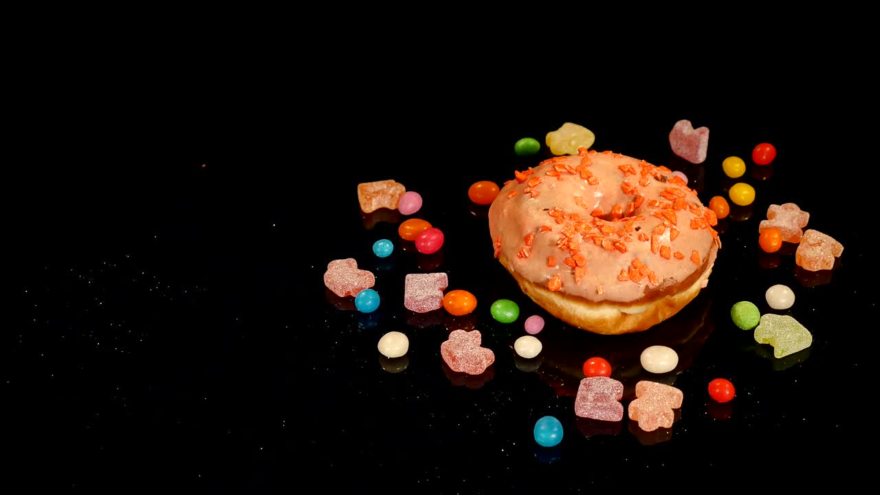 gracioso sorpreso rosquilla esmaltada con salpicaduras, dulces de caramelo a rayas, dragee colorido con pasas o cacahuetes en el interior girar sobre fondo negro