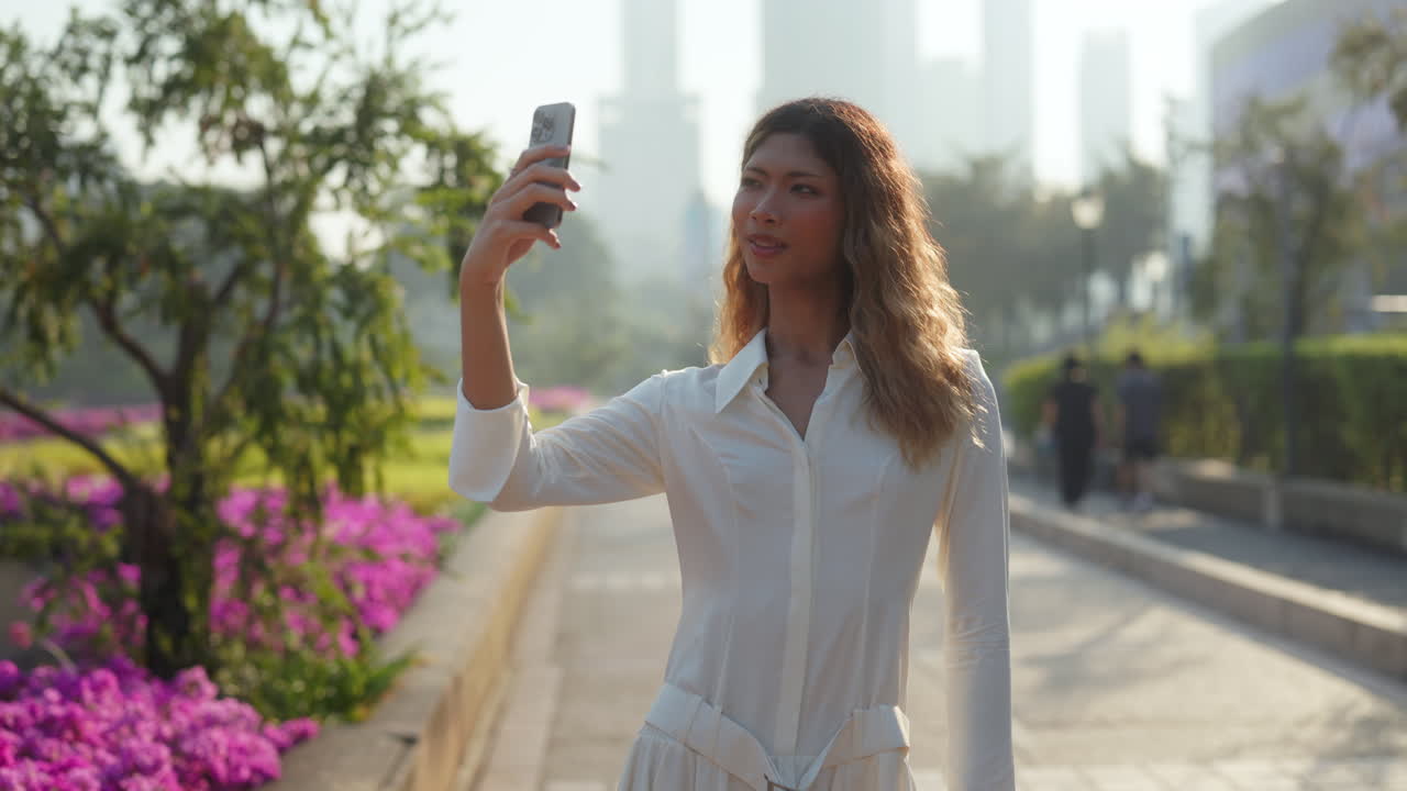 Mujer joven tomándose una selfie y usando su smartphone al aire libre en un parque de la ciudad.