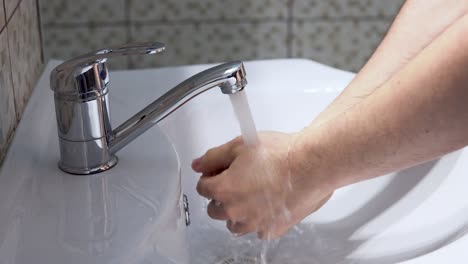 Hombre-Enjuagándose-Las-Manos-Con-Agua-Fría-En-El-Baño