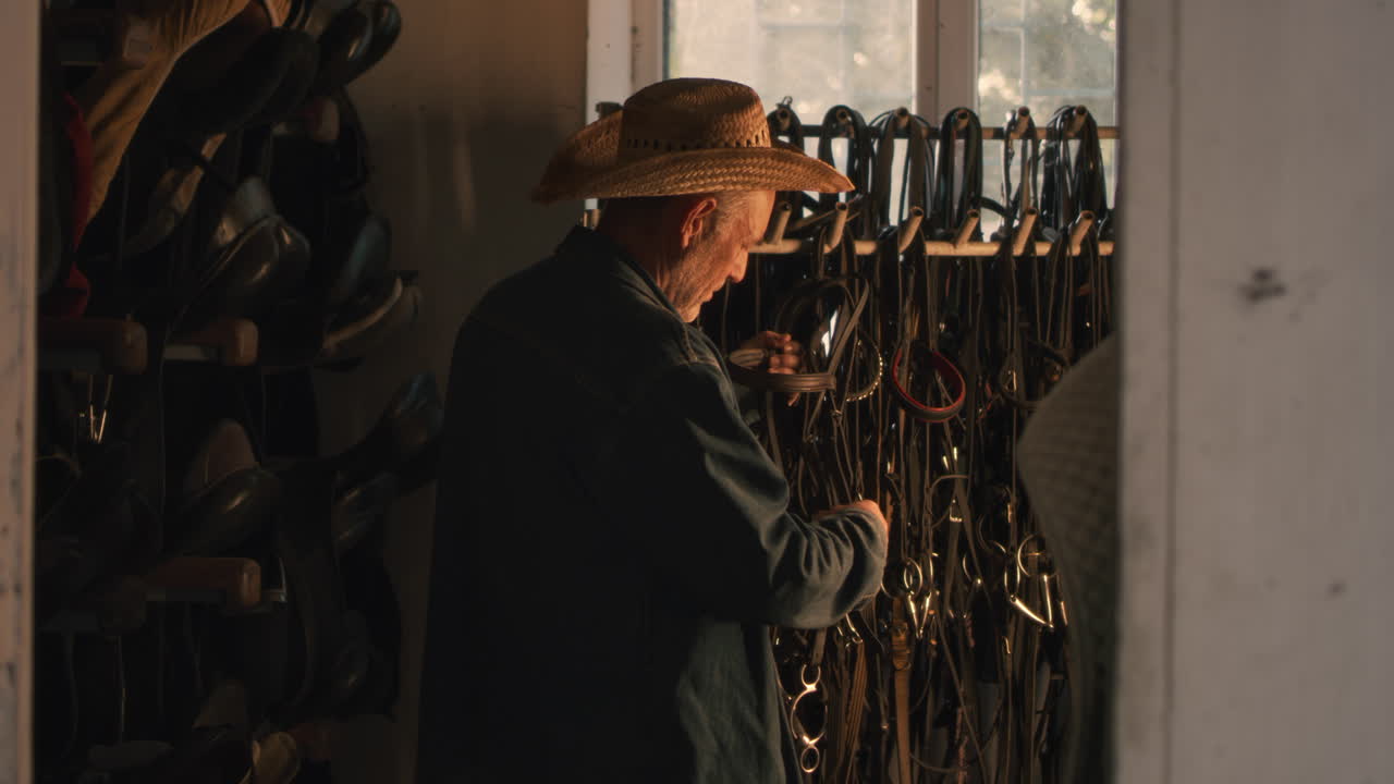 Man in a stable looking at horse tack