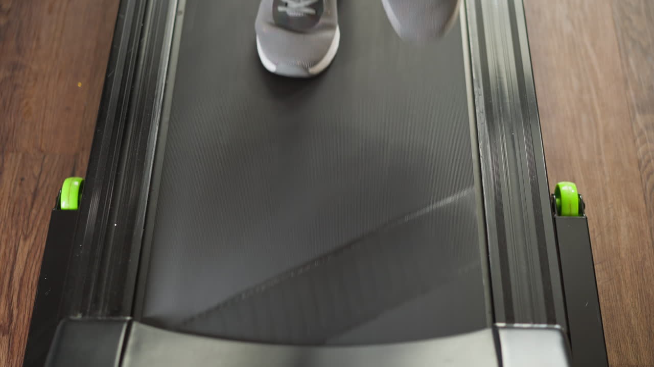 Woman uses in-home treadmill closeup. Fit lady in sports footwear engages in jogging session on house-based exercise device slow motion. Fitness routine