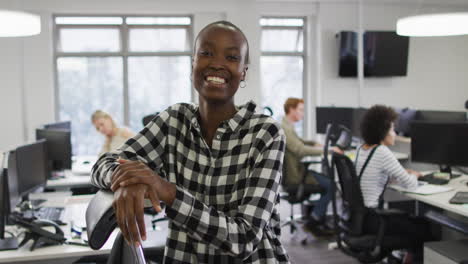 Portrait-of-smiling-african-american-creative-businesswoman-sitting-by-desk-in-modern-office