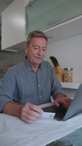 man using laptop and credit card for online shopping in the kitchen