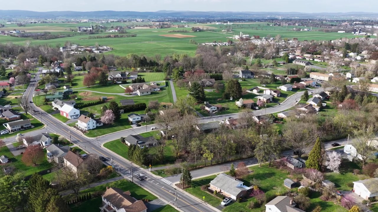 Vista aerea con drone di un tranquillo quartiere residenziale in Pennsylvania, Stati Uniti, con case residenziali, strade che si intersecano e terreni agricoli sullo sfondo durante una tranquilla giornata di primavera. Inquadratura ampia.