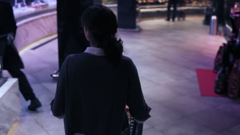 Backside-footage-of-a-female-costumer-with-curly-hair-walking-down-the-aisle-in-a-supermarket-trying-to-decide-what-to-buy