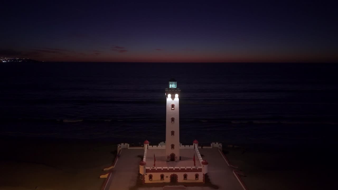 Aerial dolly shot toward the isolated La Serena Lighthouse at night with a trail of the last rays of sunset on the Pacific Ocean, northern Chile