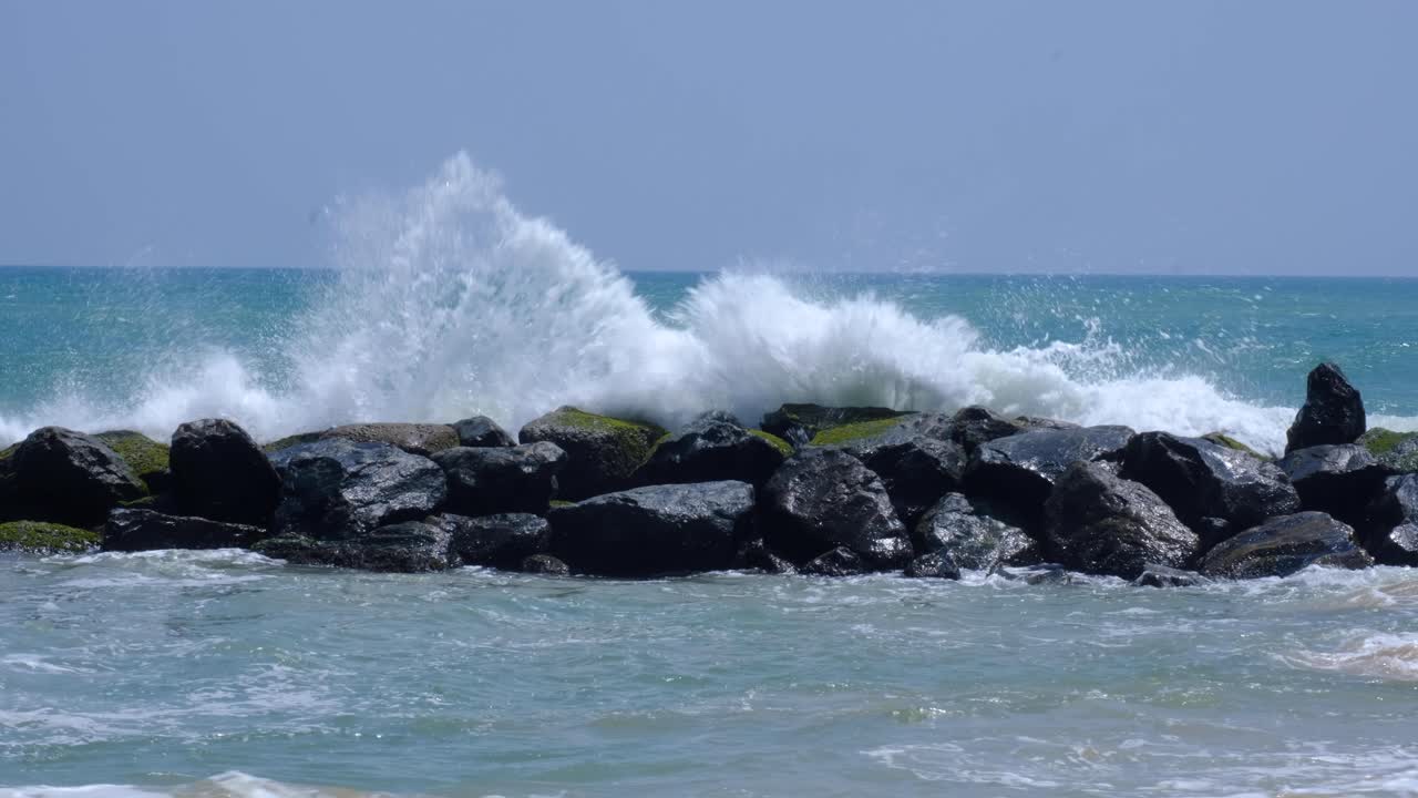 Slow motion of frothy water ocean waves crashing and splashing over rocky stone seawall in southern Sri Lanka