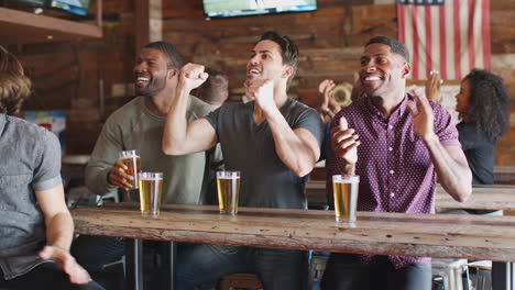 group of male friends celebrating whilst watching game on screen in sports bar
