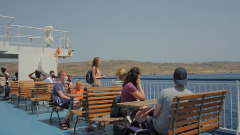 tourists in masks viewing seascape from channel ferry cruising across the sea in gozo, malta during covid pandemic. wide shot