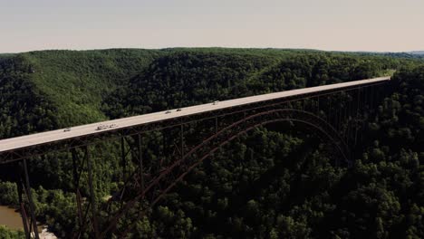 High drone shot captures New River Gorge Bridge spanning deep forest valley in West Virginia, showcasing scenic views, steel structure, and cars moving across the elevated highway