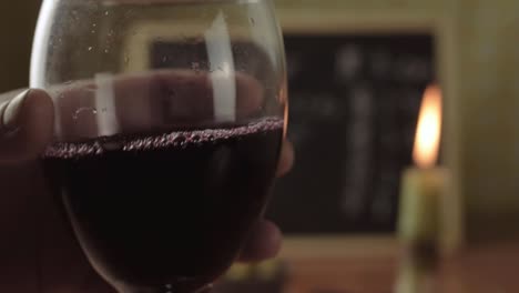 mano sosteniendo una copa de vino tinto con fondo de vela de cerca