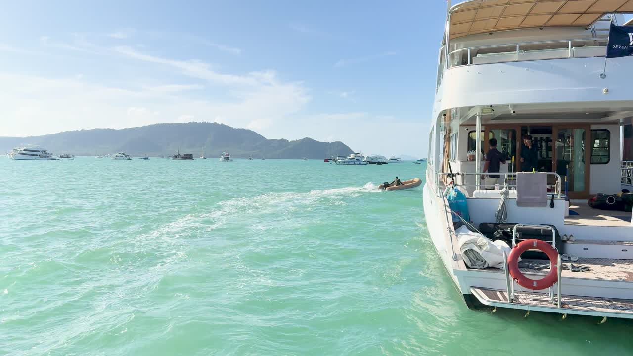 Motor yacht and dinghy traverse turquoise waters under clear skies in Chalong Bay, capturing serene maritime activity