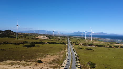 aerial view of narrowed road in countryside leading to natural mountains landscape driving through windmill turbine farm plant for green sustainable energy production