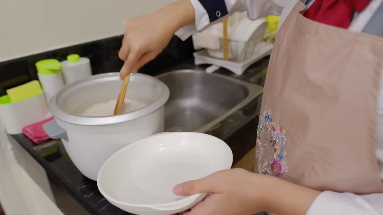 Close-up shot of a young woman wearing an apron scoops hot rice from a rice cooker