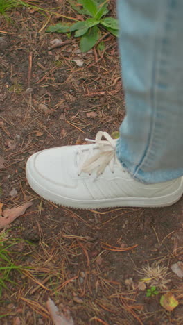 primer plano de dos individuos caminando por el sendero del bosque en vaqueros azules, uno con zapatillas negras y el otro con zapatillas blancas, la escena captura el suelo del bosque de tierra cubierto de agujas de pino, hojas esparcidas