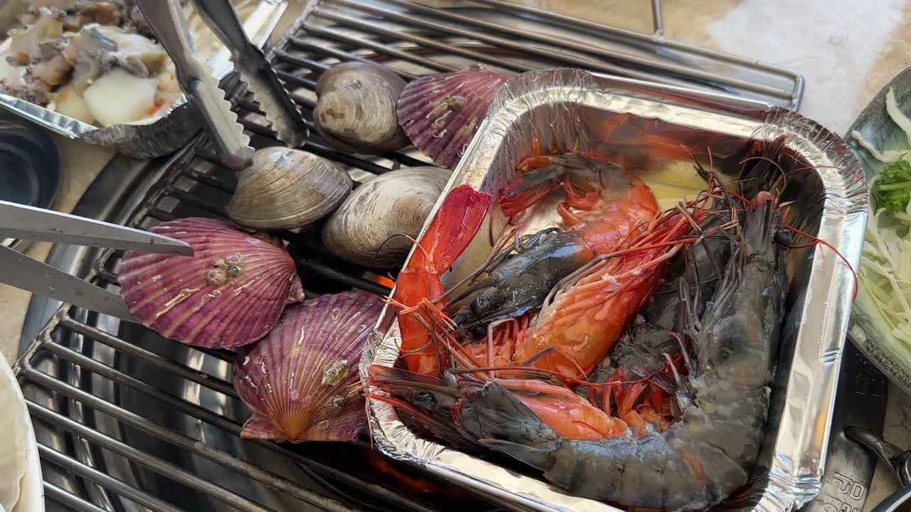 Famous restaurant in Haeundae Beach, Busan, South Korea. Server cooking fresh shellfish (shrimp, scallops, and clams) over a hot charcoal grill