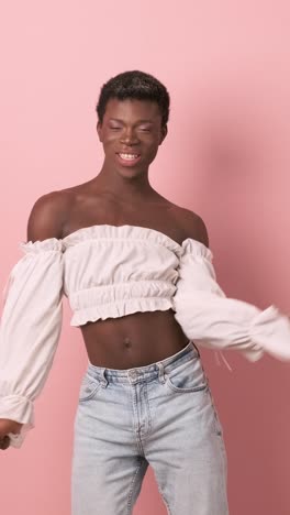 transgender casual african person dancing while looking at camera on pink background