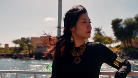 Elegant-asian-woman-on-a-boat-trip-in-Egypt-enjoys-warm-sun-rays-on-a-windy-day