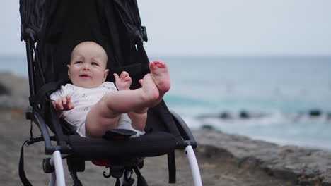 on a sandy beach, a baby in a stroller gazes tranquilly into the boundless expanse of sea waves, absorbed in the serene beauty of a late summer evening by the sea