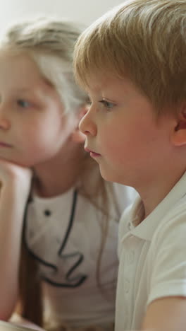 children study together using laptop. girl leans towards boy sharing ideas secretly slow motion. couple of schoolchildren learns sitting at desk in room closeup