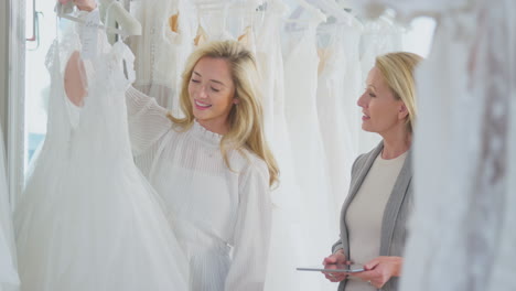 sales assistant with digital tablet helping woman to choose wedding dress in bridal store