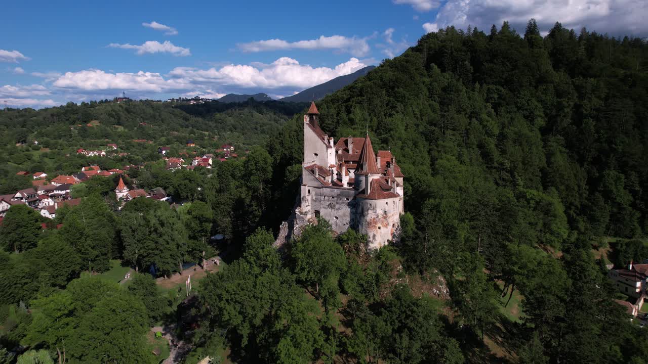 Scenic aerial shot slowly orbiting around Bran Castle. Medieval architecture among the green hills and forests of Transylvania.