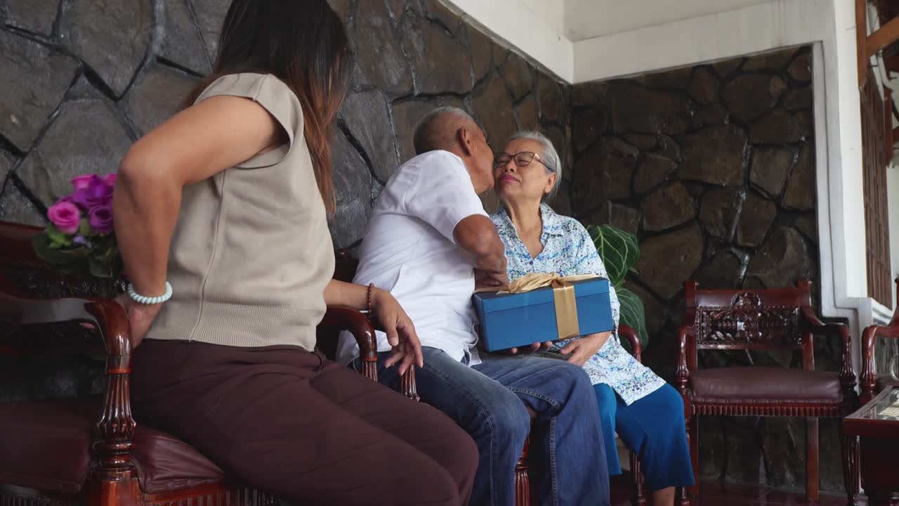madre asiática mayor feliz y hija adulta sorprende al padre con una caja de regalos y flores en su cumpleaños especial y lo besan