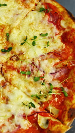 tasty pizza in restaurant. fresh round pizza with cheese and green sprouts on top rotating on a wooden board on a table. ready pizza without one part portion. close-up. vertical video