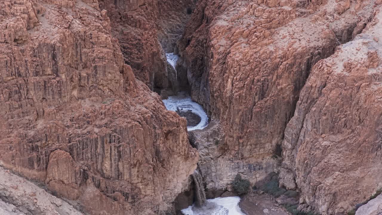 Høye vinkler på dronebilder av fossefall som renner gjennom en dyp, rød fjellkløft i Judea-ørkenen nær Dødehavet, Israel