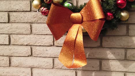 tilt-up,-close-up,-sunlight-glints-off-the-gold,-bow-on-the-end-of-a-Christmas-Wreath