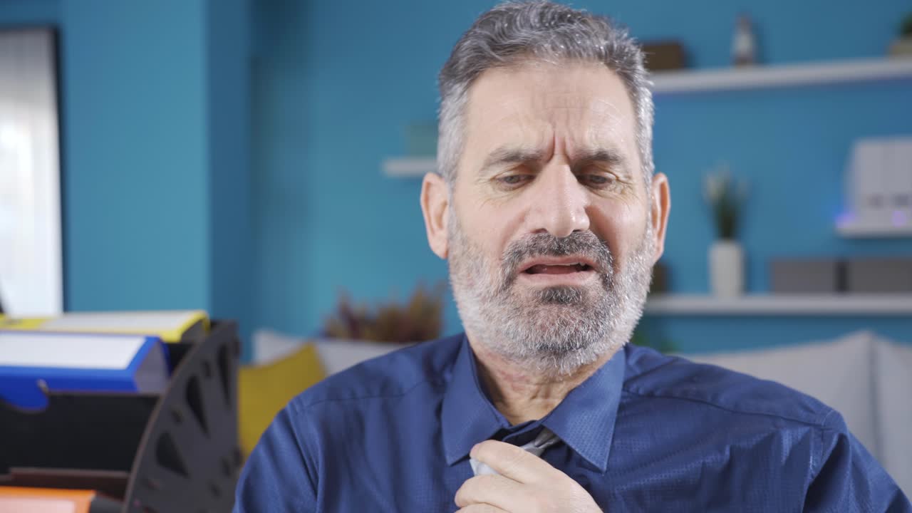 hombre de negocios maduro deprimido trabajando desde casa, recibiendo noticias tristes y aflojando su corbata.