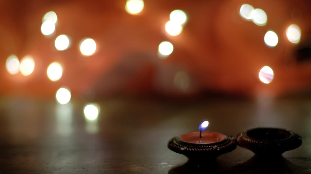 Static shot of human hand lighting traditional wax candles diya with out-of-focus bokeh background during the celebration of Hindu festival of lights or Diwali or Deepawali