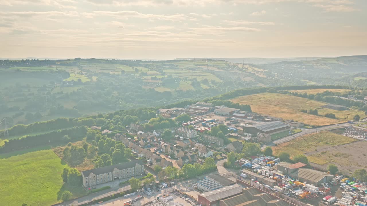 Aerial overview of Sunderland Way, Brighouse, Calderdale, West Yorkshire, England, shows rolling hills, light industry, scattered homes, and farmland under hazy afternoon