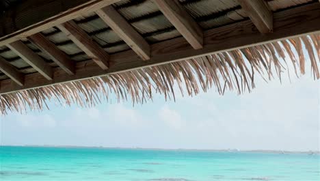 wooden roof structure of a hut with palm leaf roof overlooking a turquoise blue sea