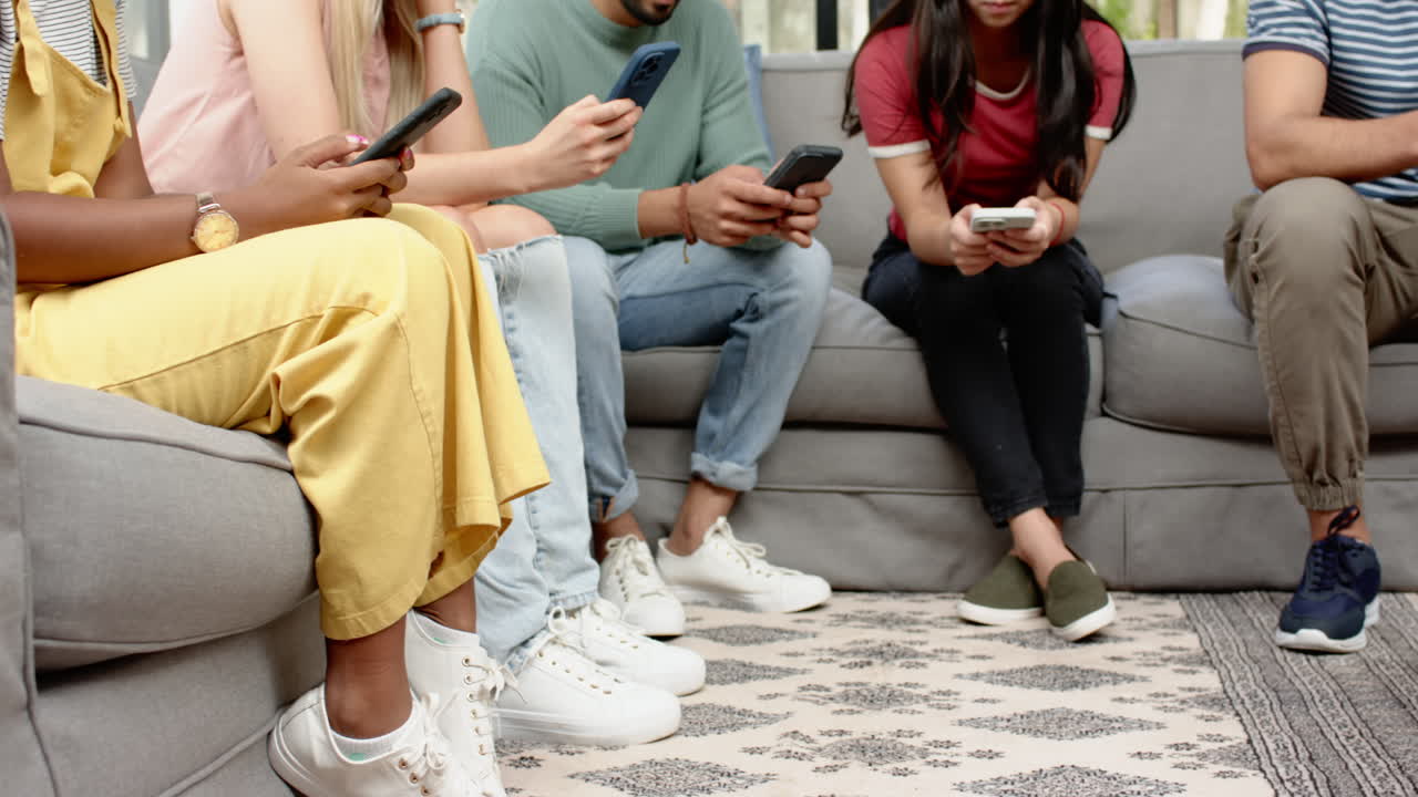 Using smartphones, group of young friends sitting on sofa together