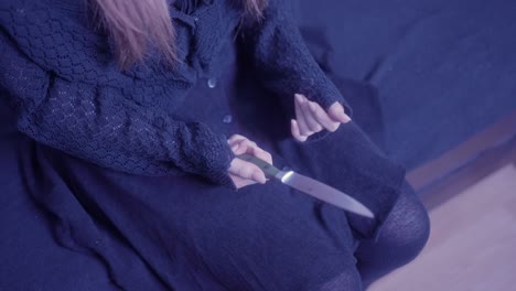 girl is thinking with a knife in her hand on the bed whether to hurt herself or not