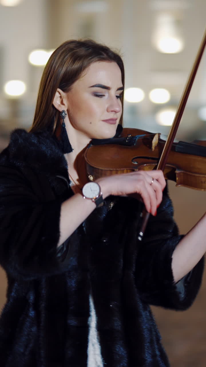 Street artist violinist girl. Young elegant woman violinist playing violin on the street at night. Vertical video