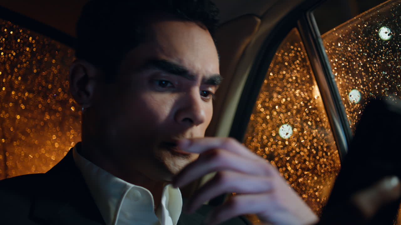 걱정스러운 감독이 비가 내리는 차 창문 근접에서 전화 화면을 보고 있습니다.