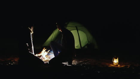 young couple roasts marshmallows on sticks around the campfire and tents that light up at night