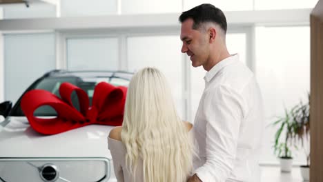 un hombre sorprende a una mujer rubia, cierra los ojos de la mujer desde atrás - coche nuevo con arco rojo, cámara lenta