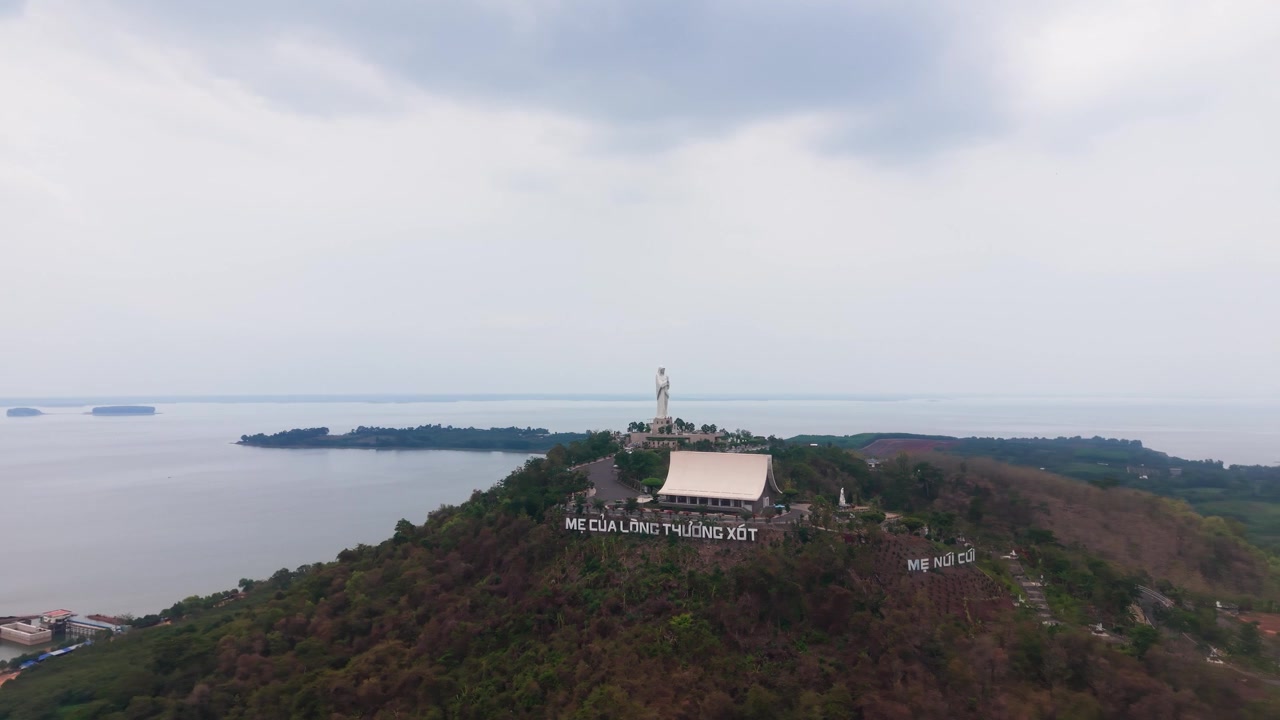 Vedute del Lago Tri An a Dong Nai, Vietnam, mostrano colline, acqua e una struttura su una collina. Nuvole coprono il cielo mentre si vedono barche sull'acqua sottostante.