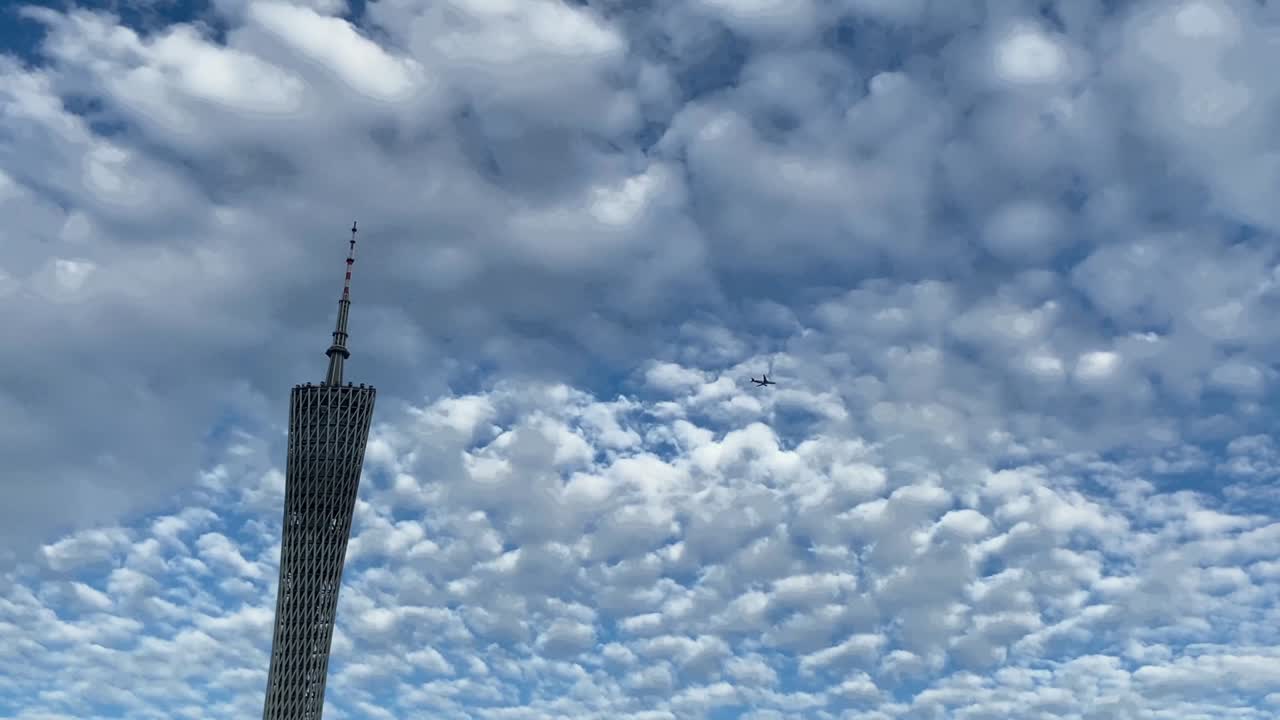 비행기는 푸른 하늘과  구름에 대항하여 광저우 타워를 날아갑니다.