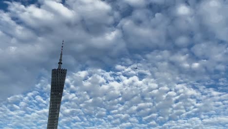 el avión vuela sobre la torre de guangzhou contra el cielo azul y las nubes blancas.