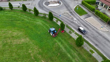 high angle view revealing farmer mowing grass with tractor near roundabout in residential area of piacenza, showcasing agricultural work amid urban italian landscape