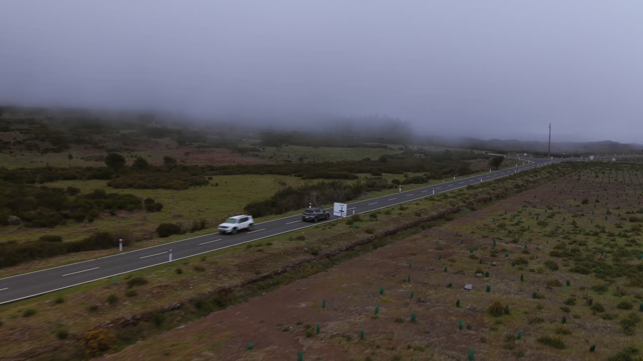 Aerial view of a car driving along a winding road near Pico do Areeiro and Pico das Torres in Madeira, Portugal, on a cloudy day