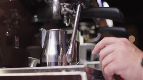 barista filling coffee can with hot water from professional shiny, silver barista coffee machine