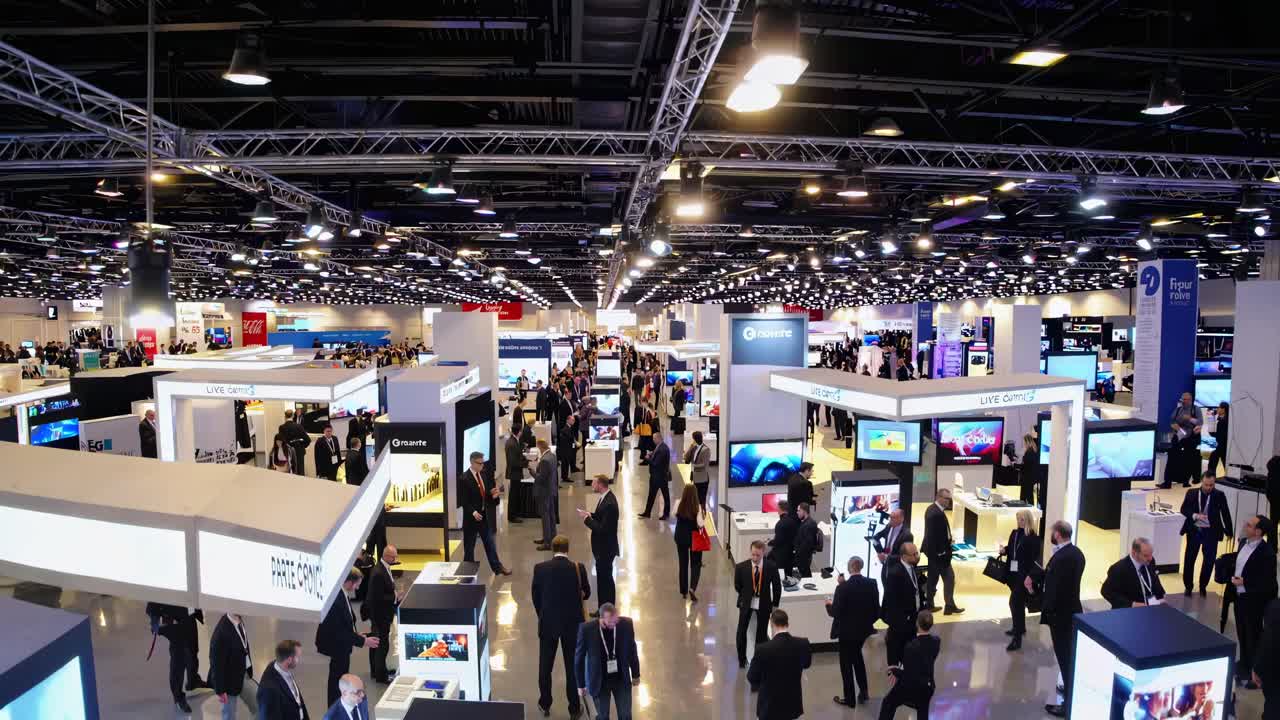 High-angle shot of a bustling trade show with numerous booths and attendees, capturing the dynamic